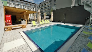 Ein Schwimmbecken mit Liegestühlen und Sonnenschirmen, umgeben von mehrstöckigen Gebäuden.
