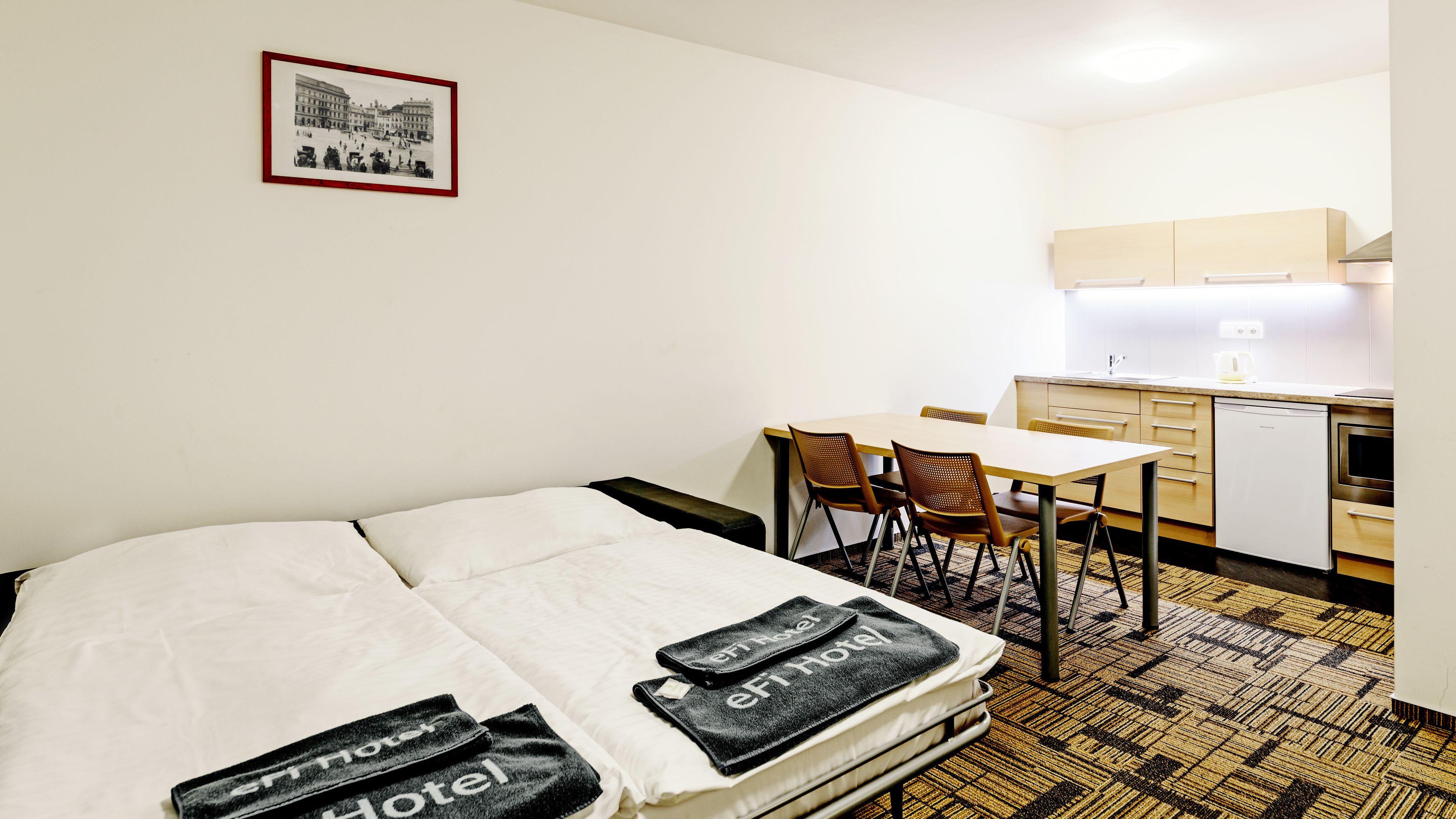 Habitación de hotel con cama, escritorio, silla, kitchenette y un cuadro en la pared.