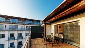 Ein Balkon mit Tisch und Stühlen, Blick auf benachbarte Gebäude und einem klaren Himmel.