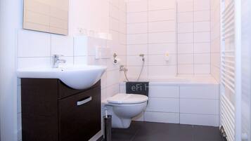 A modern bathroom with a white sink, dark wooden cabinet, white toilet, and a bathtub.