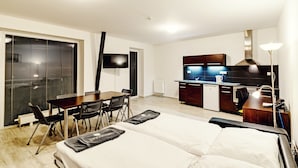 Ein modernes Hotelzimmer mit einem Bett, einem Esstisch mit Stühlen, einer Küchenzeile und einem Fernseher.
