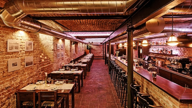 Ein Restaurant mit Backsteinwänden, freiliegenden Lüftungsrohren und einer langen Theke mit Barhocker.