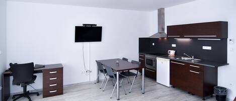 Una cocina moderna con mesa, sillas, televisión y horno empotrado.