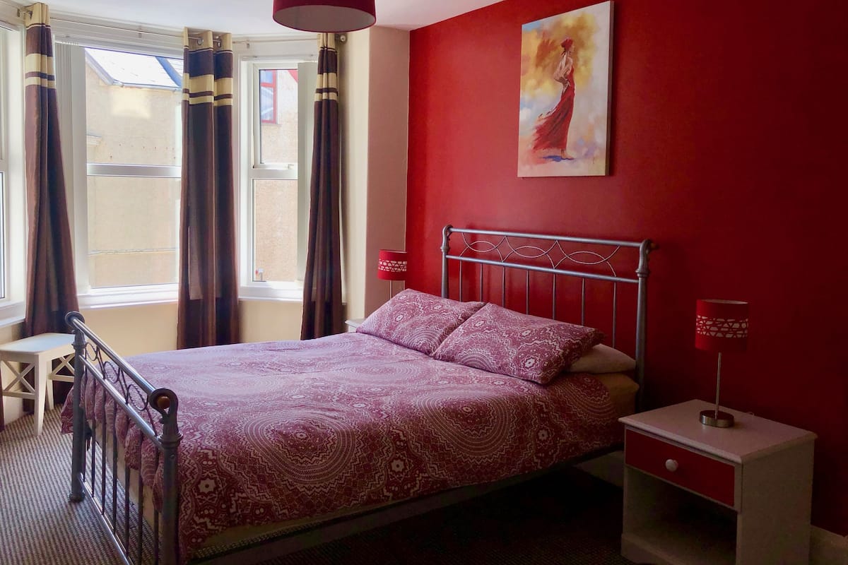 A bedroom with a bed, a nightstand, a lamp, and a painting on the wall.