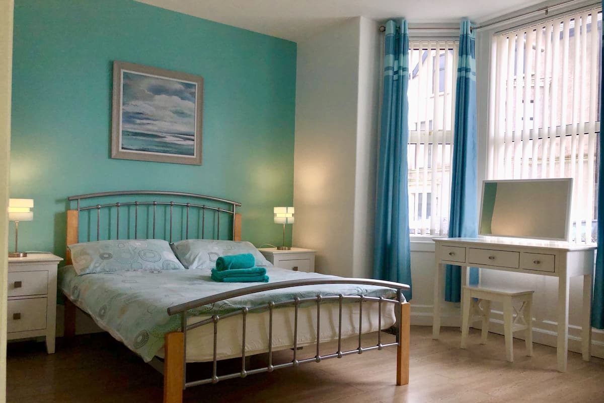 A bedroom with a bed, bedside tables, a desk, and a window with curtains.