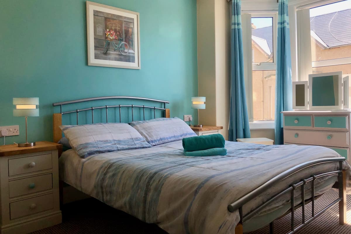 A bedroom with a bed, nightstands, a dresser, and a window with curtains.