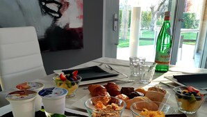 Een ontbijttafel met verschillende soorten eten, een fles Acqua Panna en een vaas met roze bloemen.