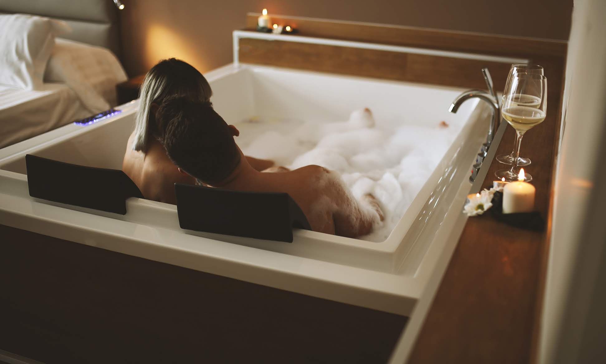 Eine Person entspannt in einer Badewanne, mit einem Weinglas und Kerzen daneben.