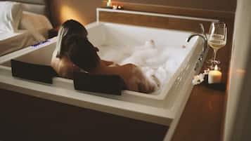 Eine Person entspannt in einer Badewanne, mit einem Weinglas und Kerzen daneben.