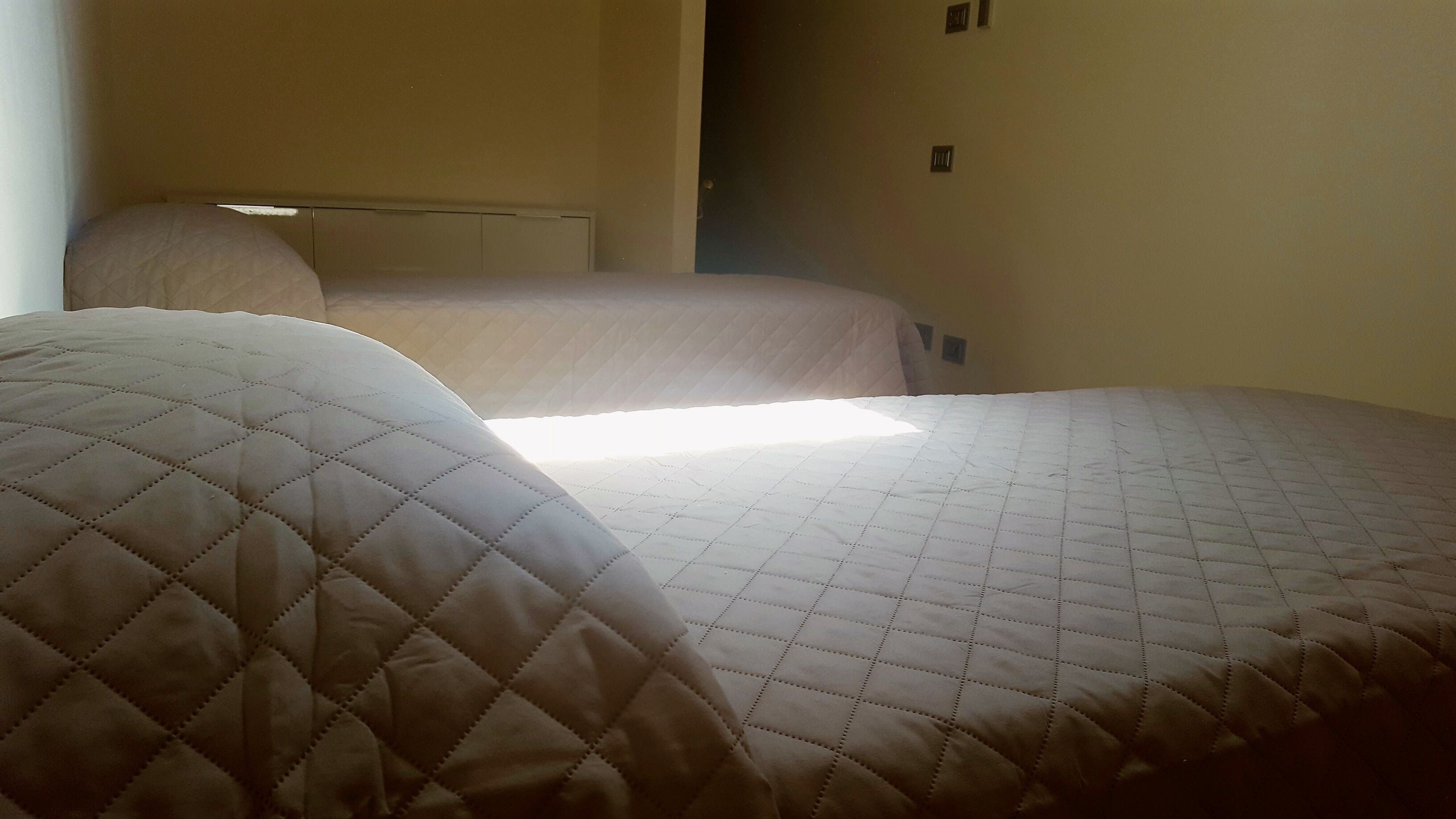 Ein Hotelzimmer mit zwei Betten, einer sichtbaren Tür und einem Lichtschalter an der Wand.