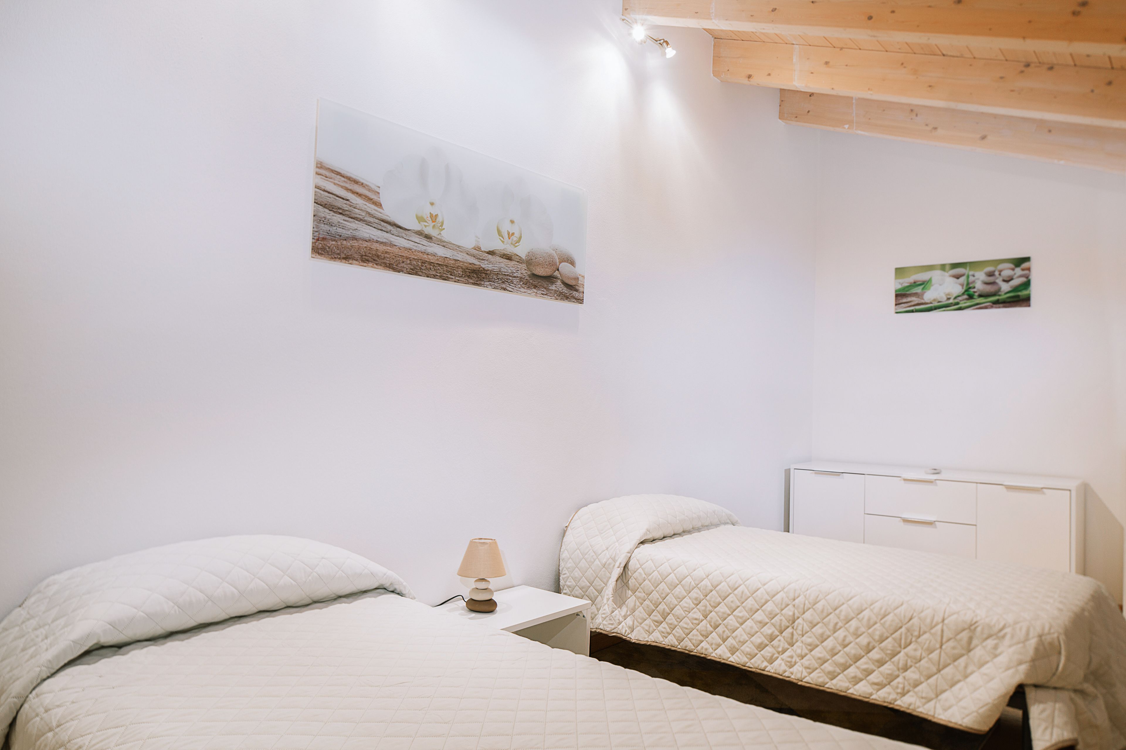 Un dormitorio con dos camas, una mesita de noche con lámpara y un cuadro en la pared.