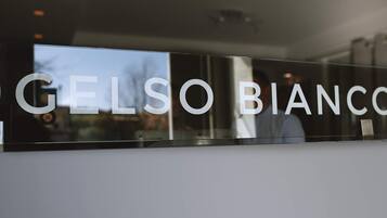 Una ventana de vidrio que refleja a una persona y un edificio, mostrando el texto "CELSO BIANCO".