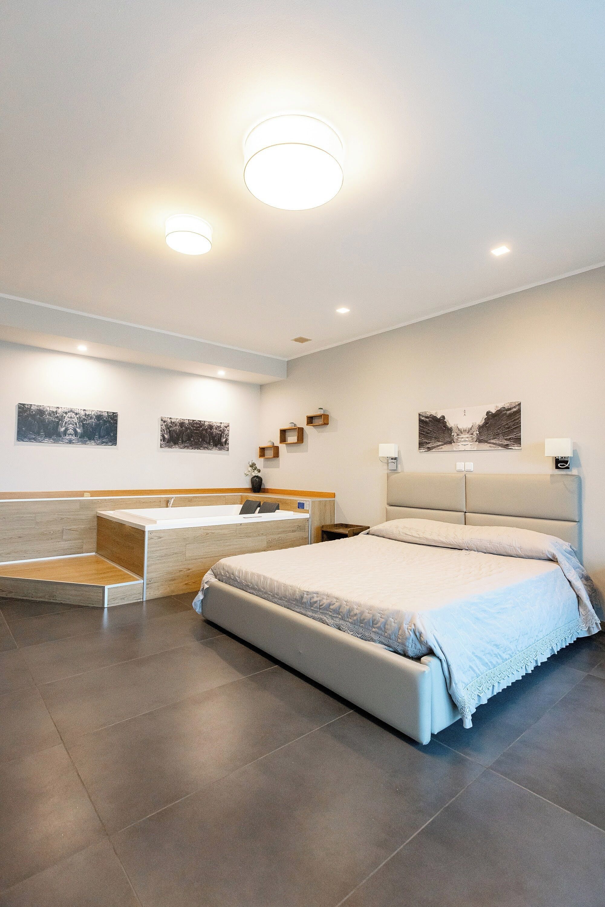 A modern bedroom with a large bed, a bedside table, a built-in bench, and two wall-mounted lamps.