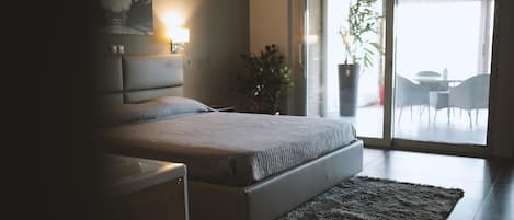 A modern bedroom with a bed, bedside table, lamp, and a view of the outdoors through a glass door.
