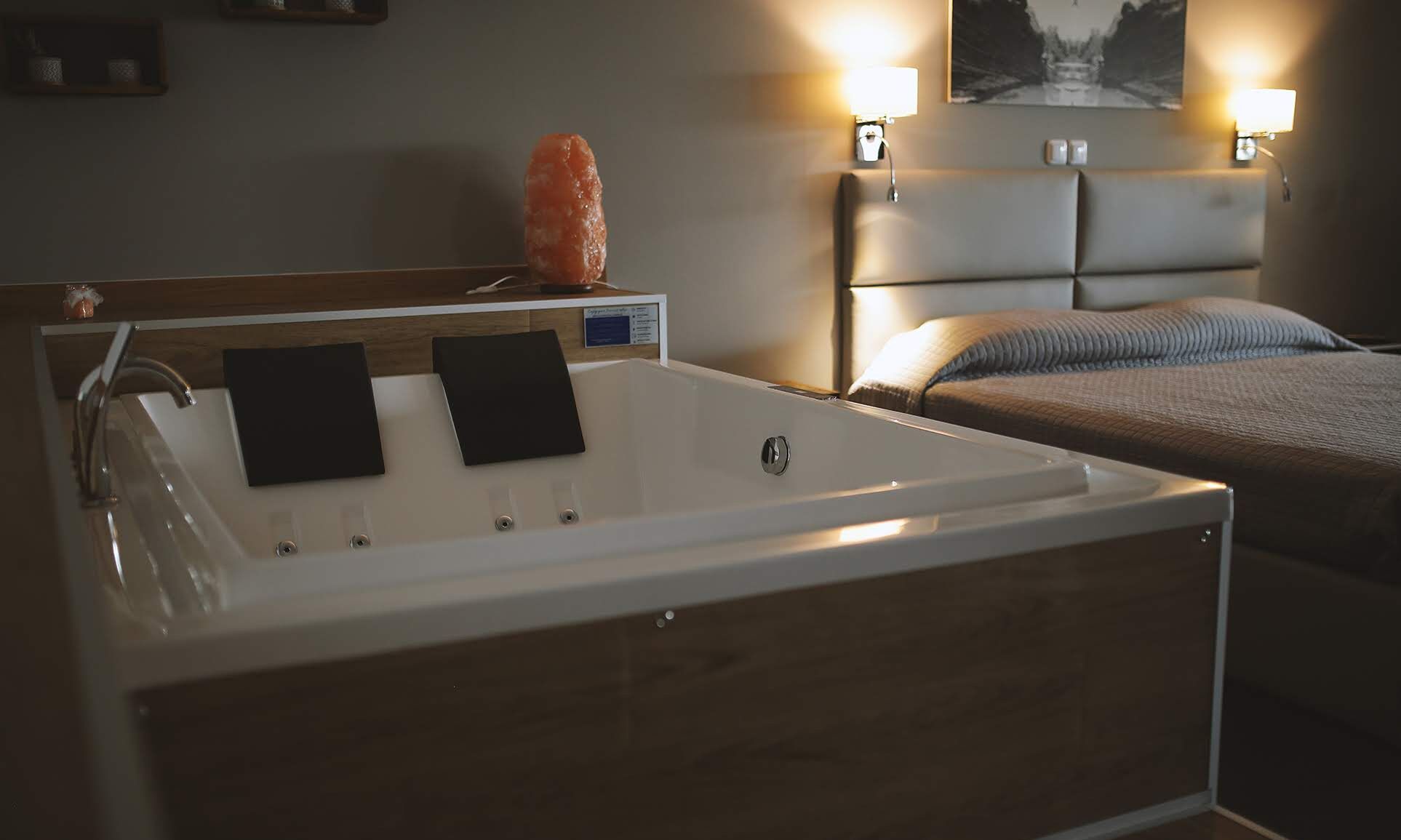 Une salle de bain moderne avec une baignoire, deux serviettes noires, un meuble-lavabo en bois et une tête de lit avec un lit en arrière-plan.