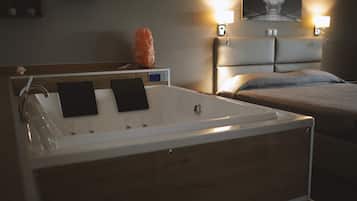 Une salle de bain moderne avec une baignoire, deux serviettes noires, un meuble-lavabo en bois et une tête de lit avec un lit en arrière-plan.