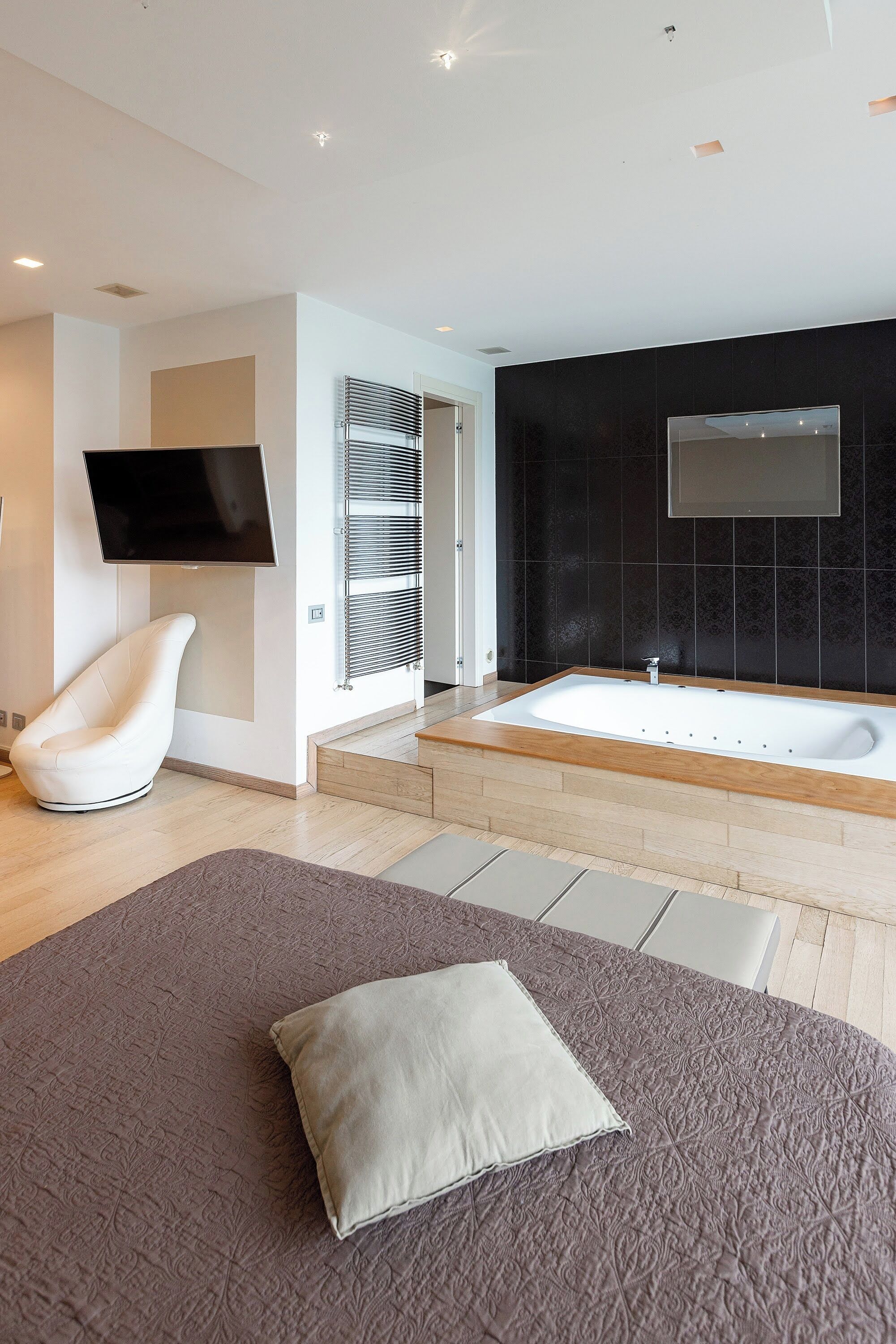 Une salle de bain moderne avec une baignoire, un téléviseur à écran plat et une chaise blanche.