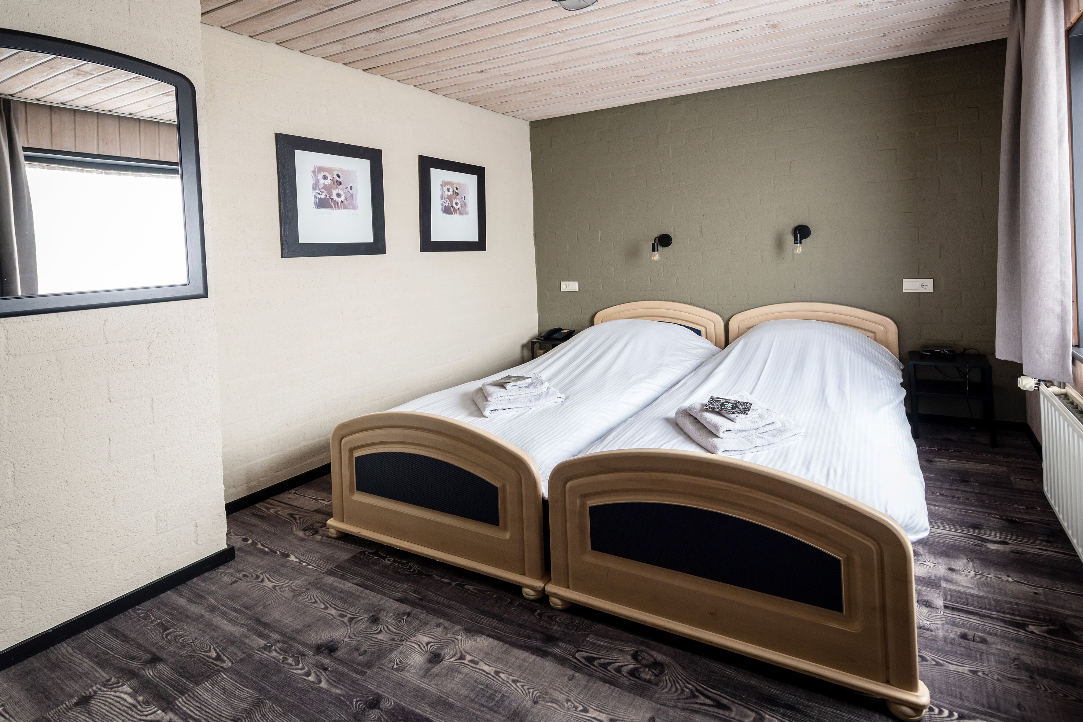 A bedroom with two wooden beds, a window with a curtain, and two framed pictures on the wall.