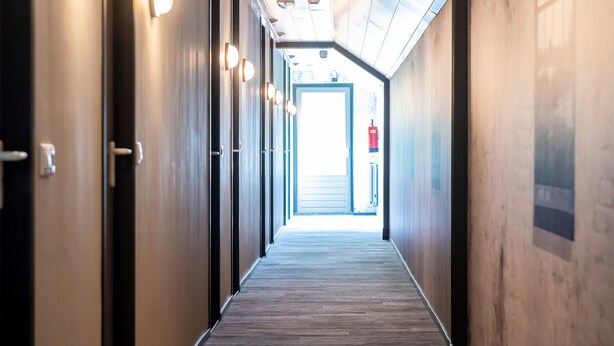 A hallway with wooden flooring, recessed lighting, and doors on both sides.