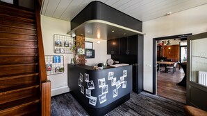 A reception area with a curved desk, a wall-mounted photo collage, and a view into a dining area with wooden flooring and furniture.