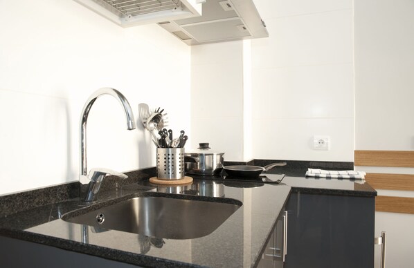 A modern kitchen with a stainless steel sink, a range hood, and a wooden countertop. - Apartamentos Sabinas Don Jaime (Zaragoza)