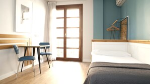 A hotel room with a bed, a desk with chairs, a window with curtains, and a wall-mounted air conditioner. - Apartamentos Sabinas Don Jaime (Zaragoza)