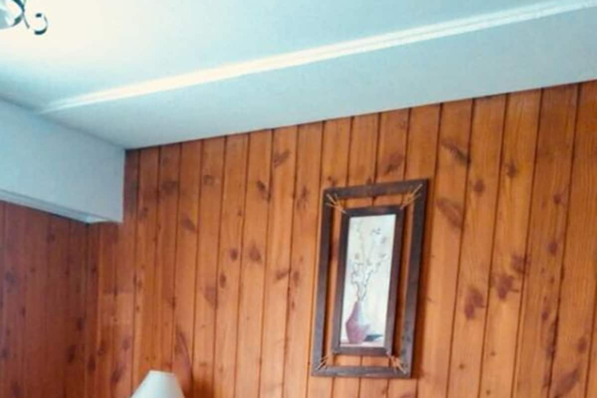 Een kamer met houten paneelwanden, een bed met een blauwe spreideken en twee wandlampen.