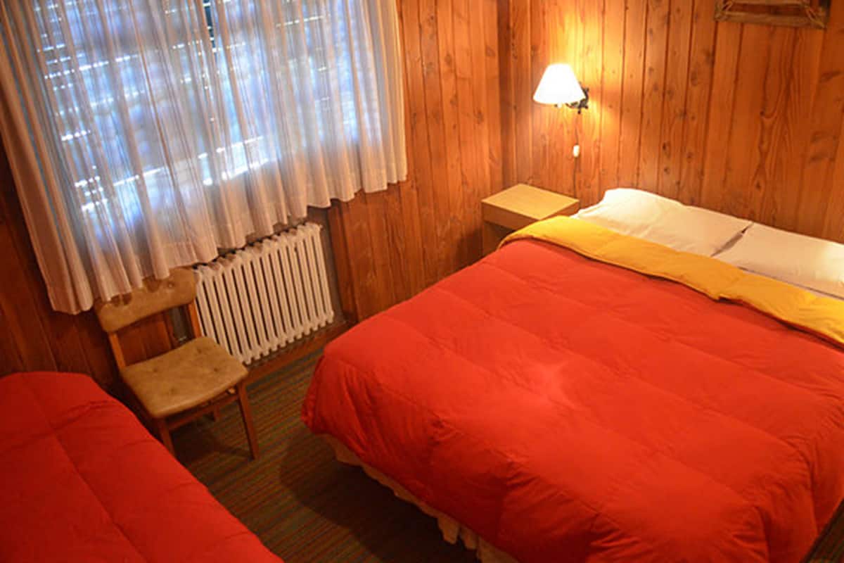 Een kamer met twee bedden, een houten vloer, een radiator, een stoel en een lamp.