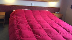 Een hotelkamer met een groot bed, een houten hoofdbord, nachtkastjes en een wandlamp.