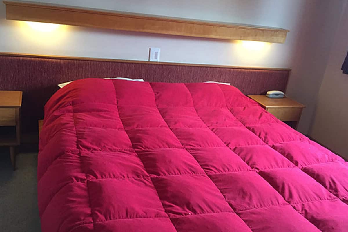 Een hotelkamer met een groot bed, een houten hoofdbord, nachtkastjes en een wandlamp.