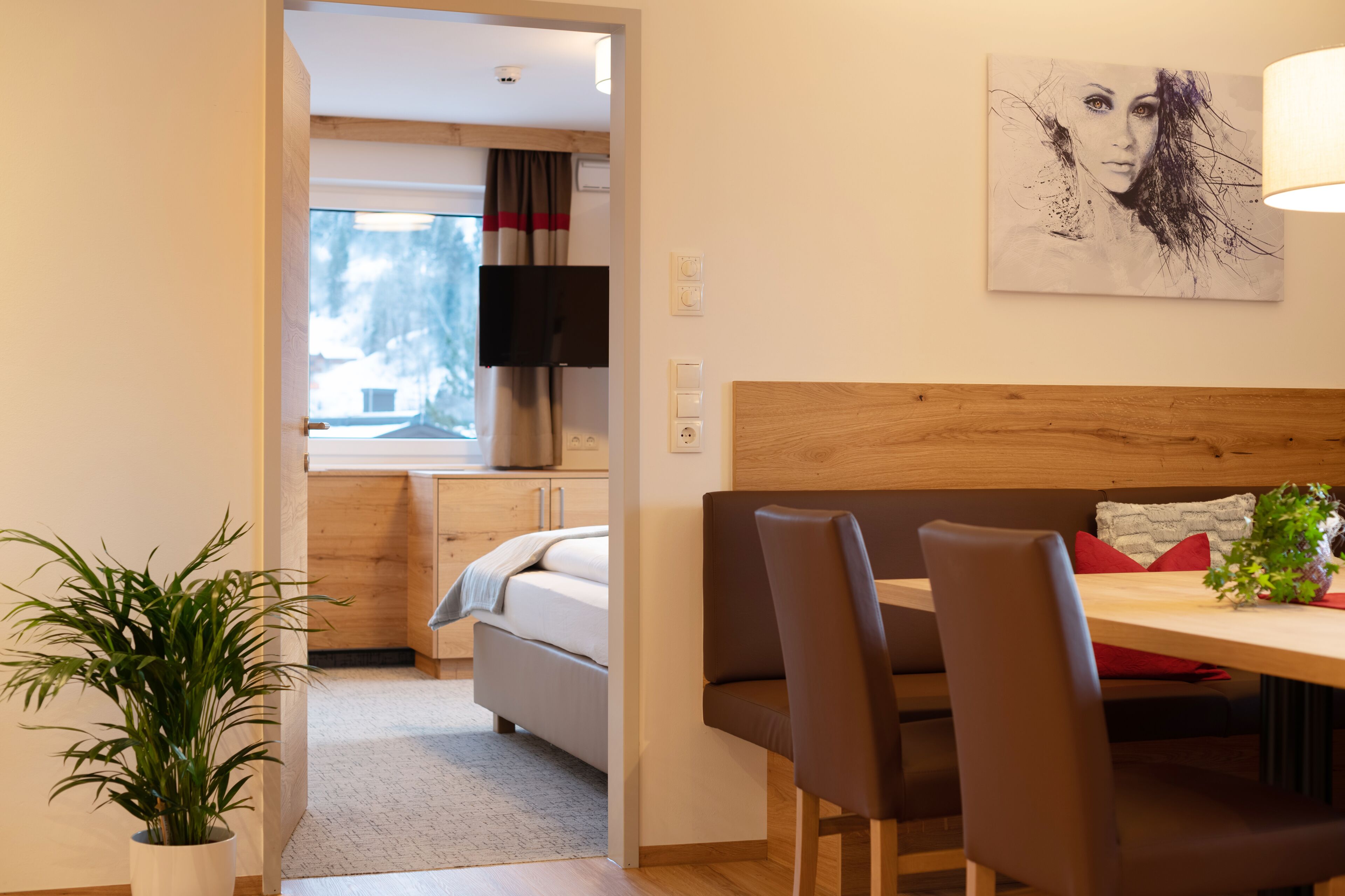 A modern room with a bed, a dining table with chairs, a potted plant, and a painting on the wall.