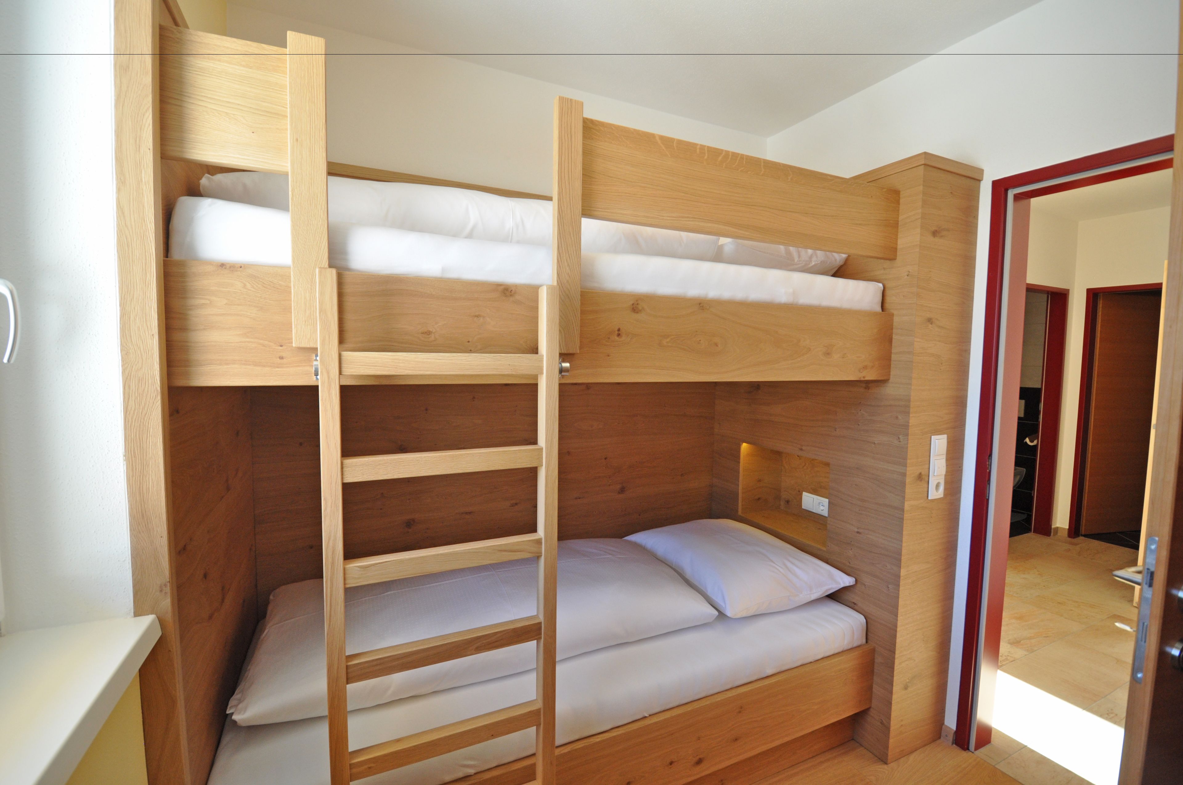A bunk bed with a ladder, wooden walls, and a door leading to another room.