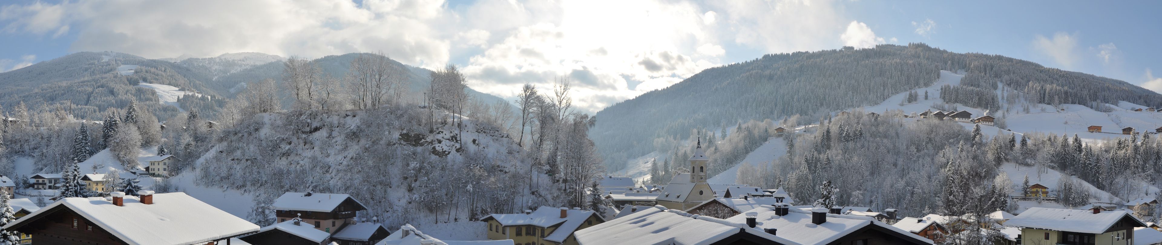 A snow-covered village with traditional wooden houses, a church, and mountains in the background.