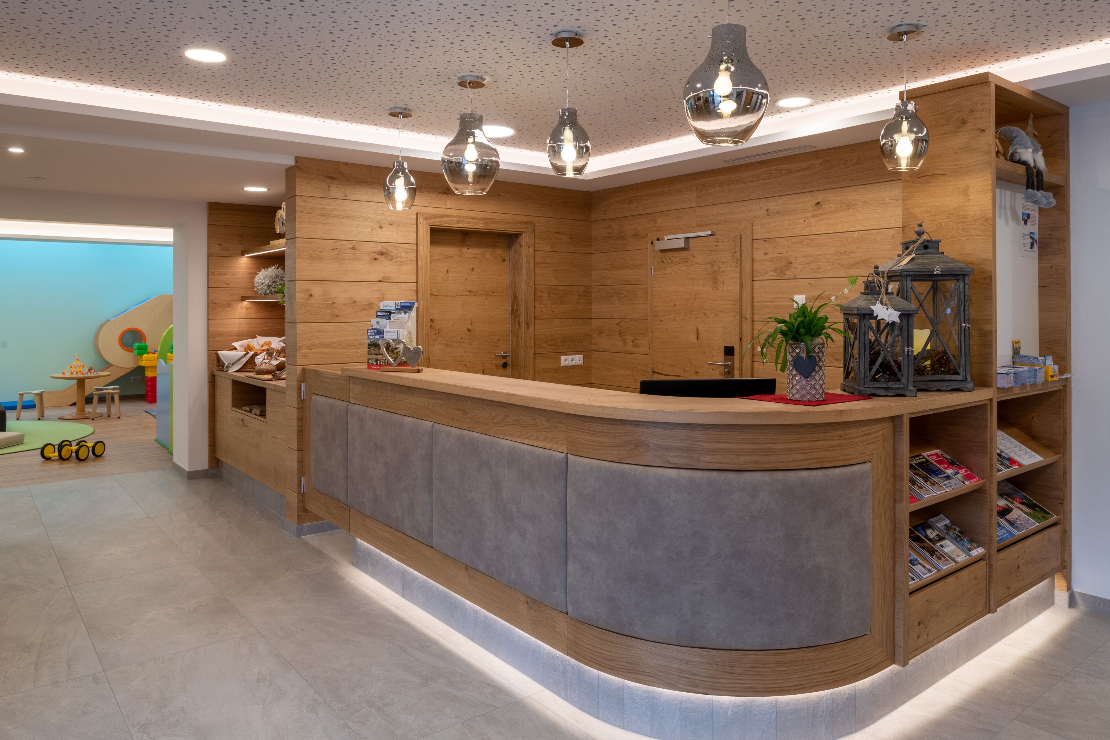 A modern reception area with a wooden reception desk, pendant lighting, and a magazine rack.