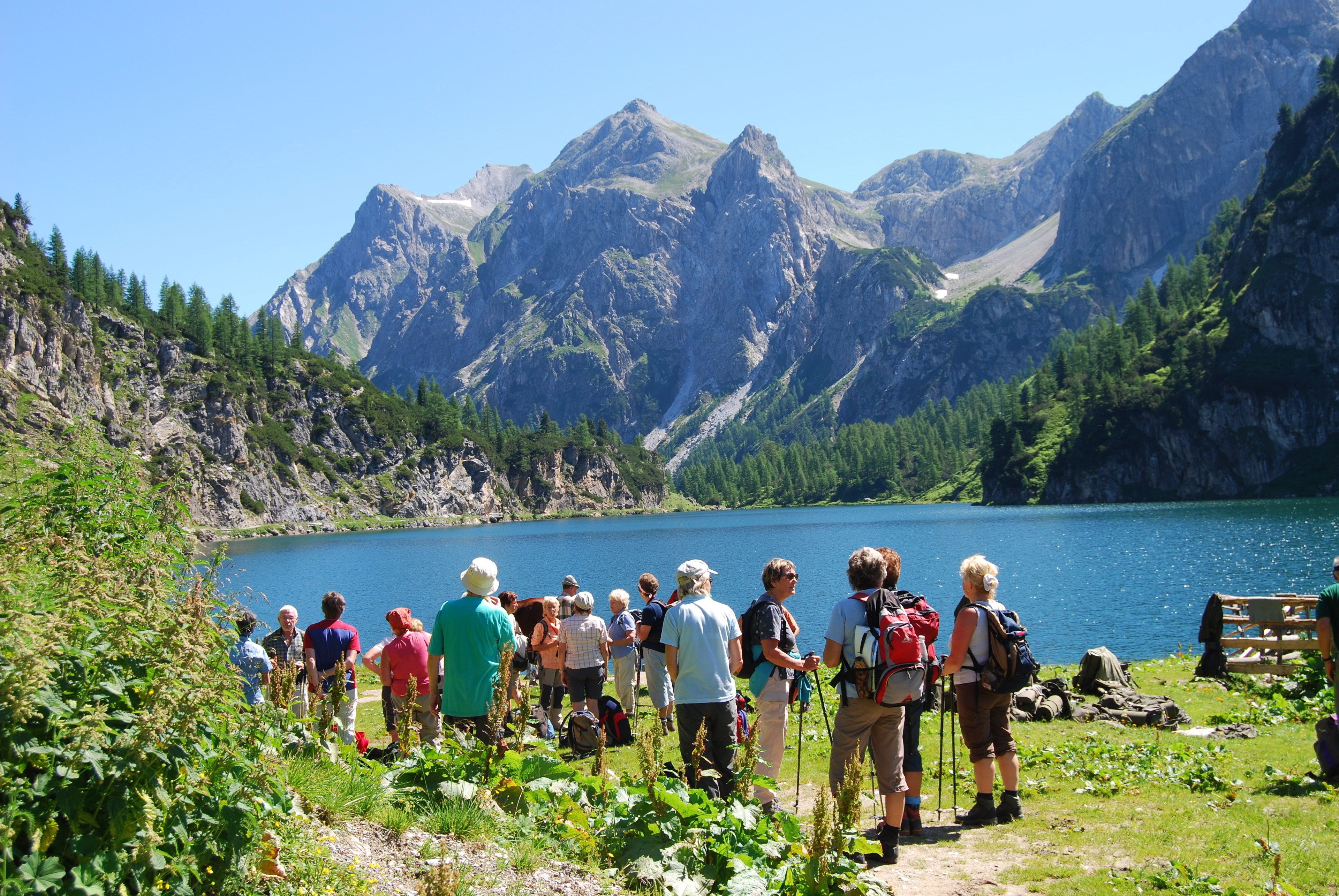 A group of people standing on a path overlooking a lake with mountains in the background.