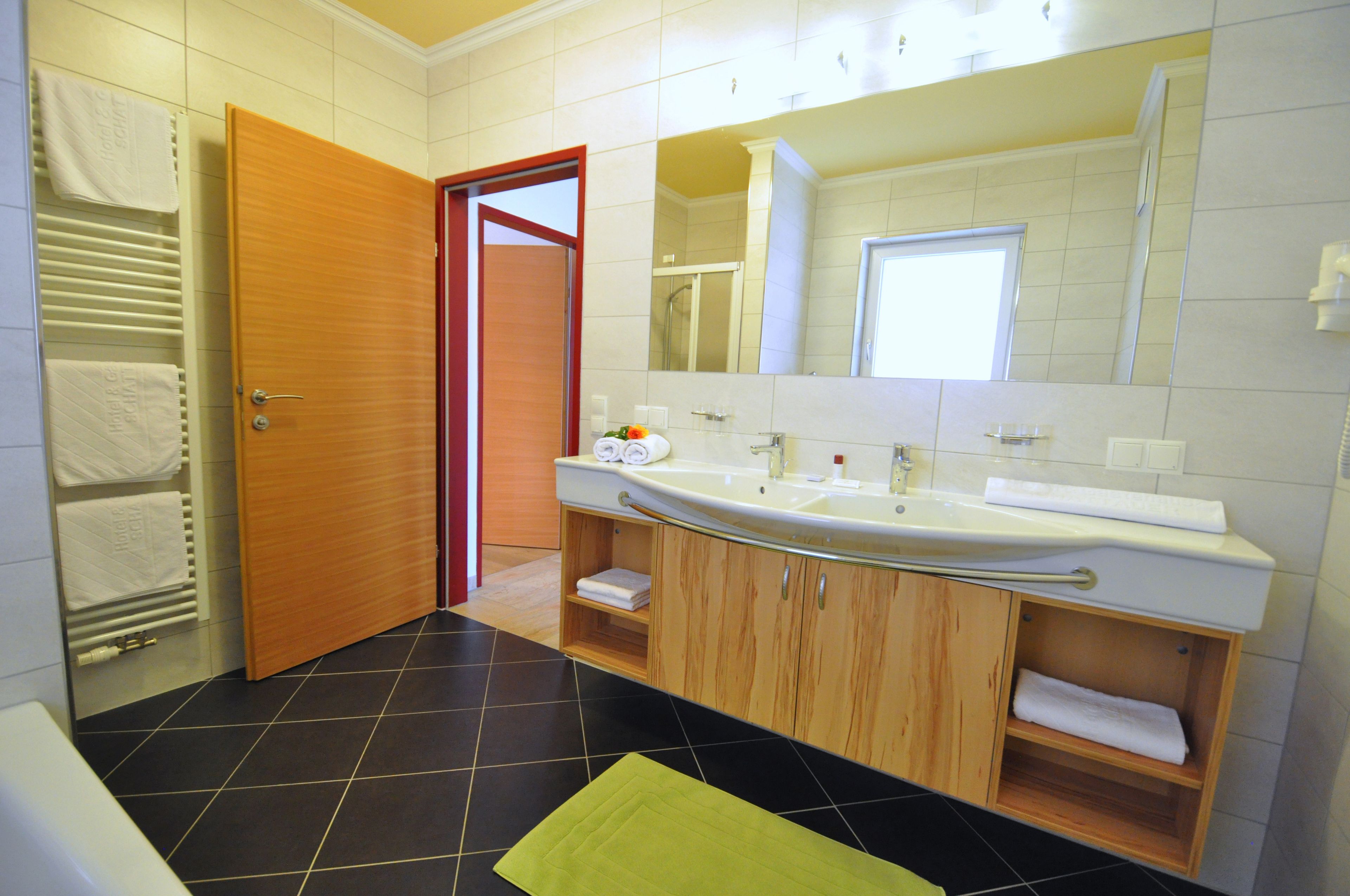 A bathroom with a wooden vanity, a large mirror, and a black and white tiled floor.