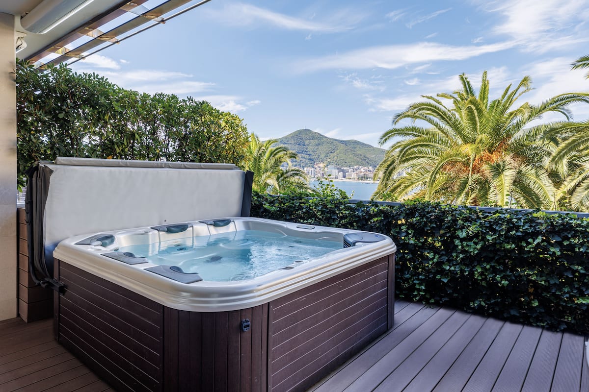 A hot tub on a wooden deck with a view of a city and mountains.