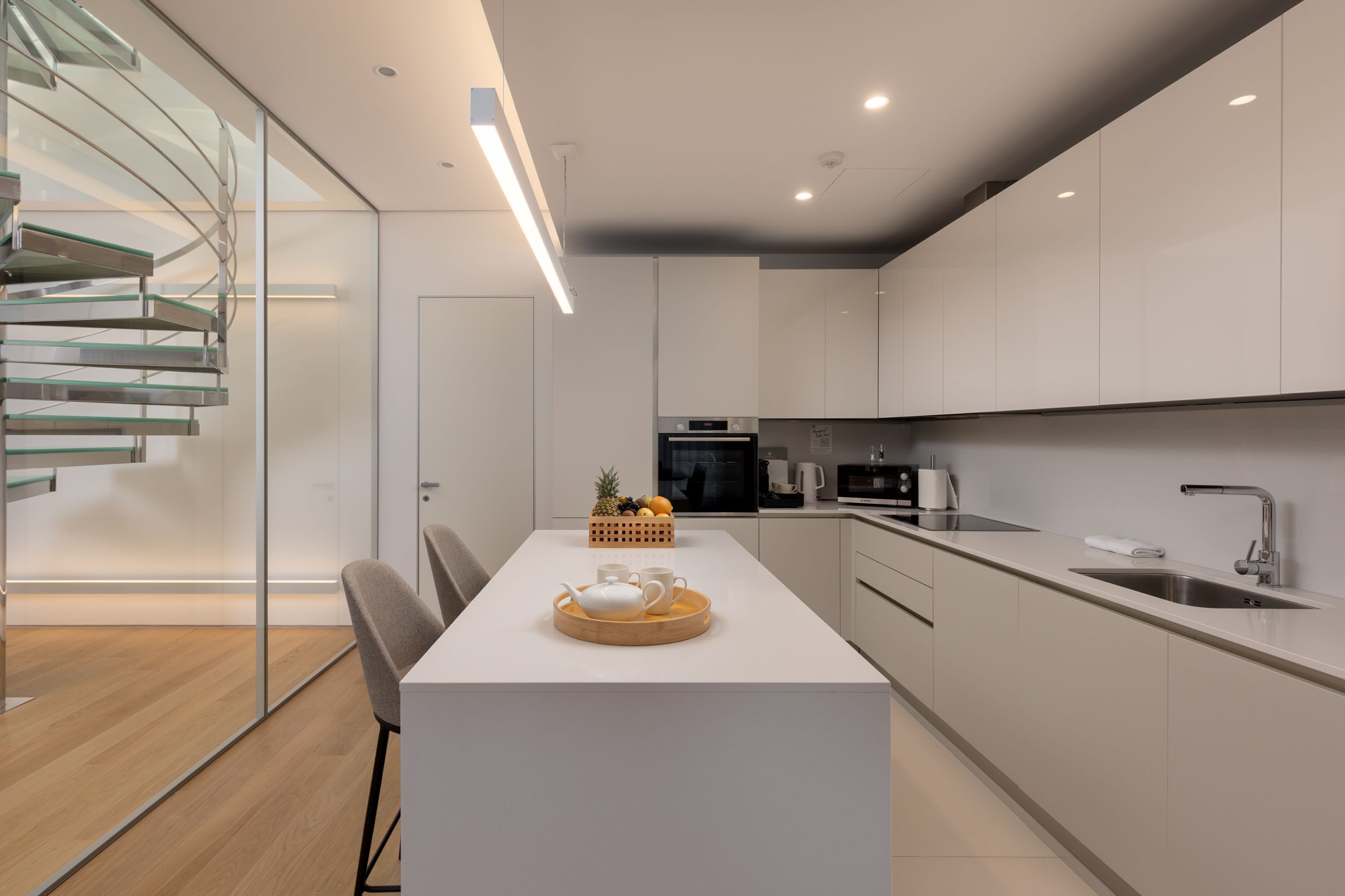 A modern kitchen with white cabinetry, a central island with a tray of fruit, and a built-in oven.