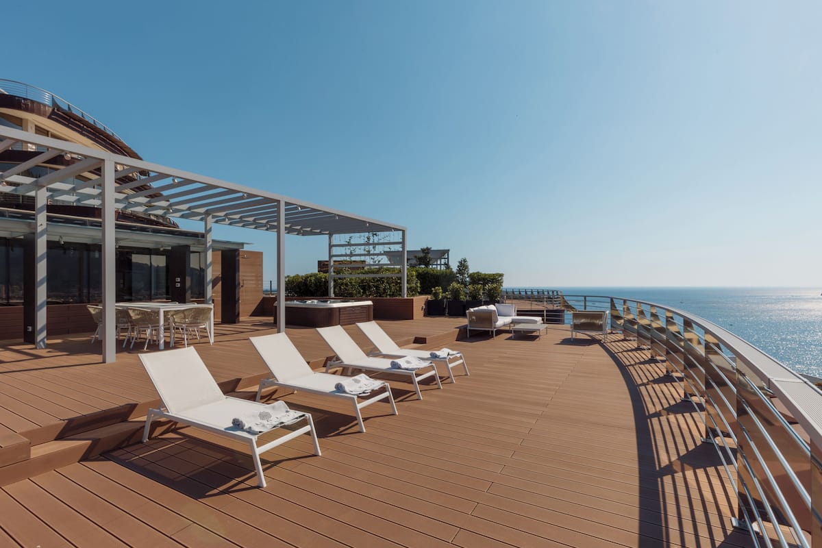 A sun deck with white lounge chairs, a covered seating area, and a view of the ocean.