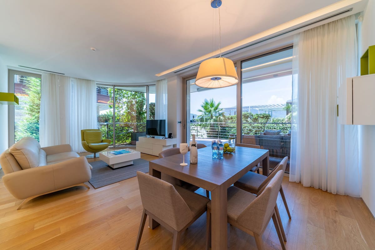 A modern living room with a dining area, large windows, and a balcony with outdoor furniture.