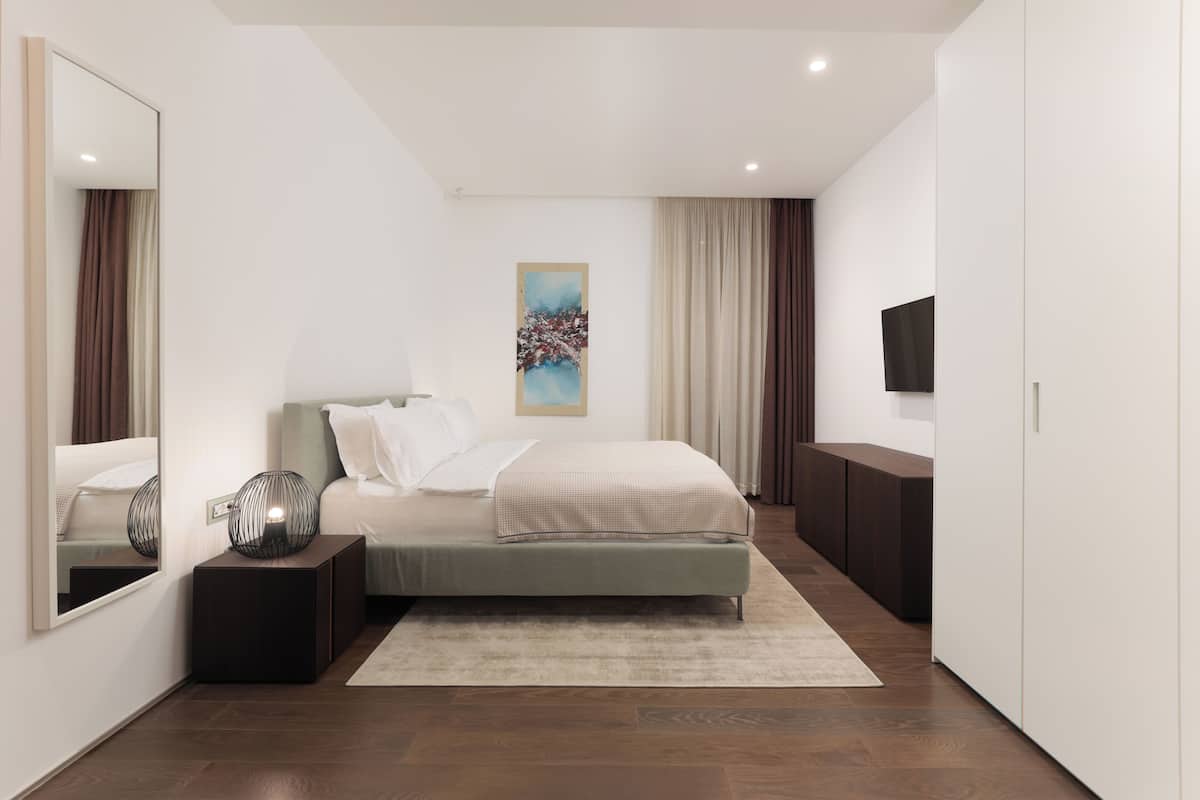 A modern bedroom with a bed, bedside tables, a mirror, a painting, and a television.