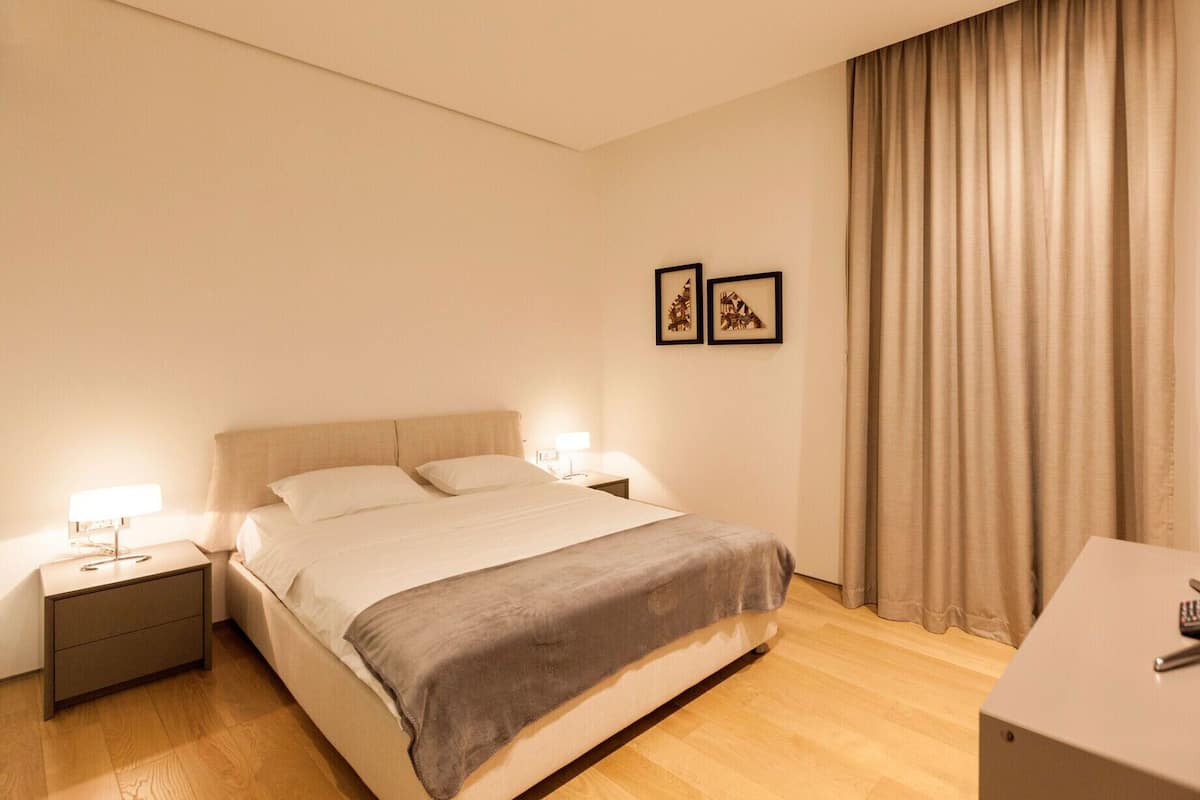 A hotel room with a bed, bedside tables, a TV, and curtains.