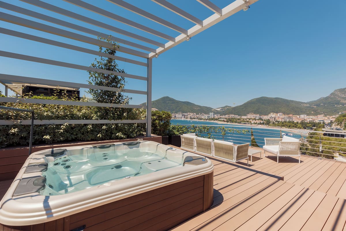 A hot tub on a wooden deck with a view of a city and mountains.