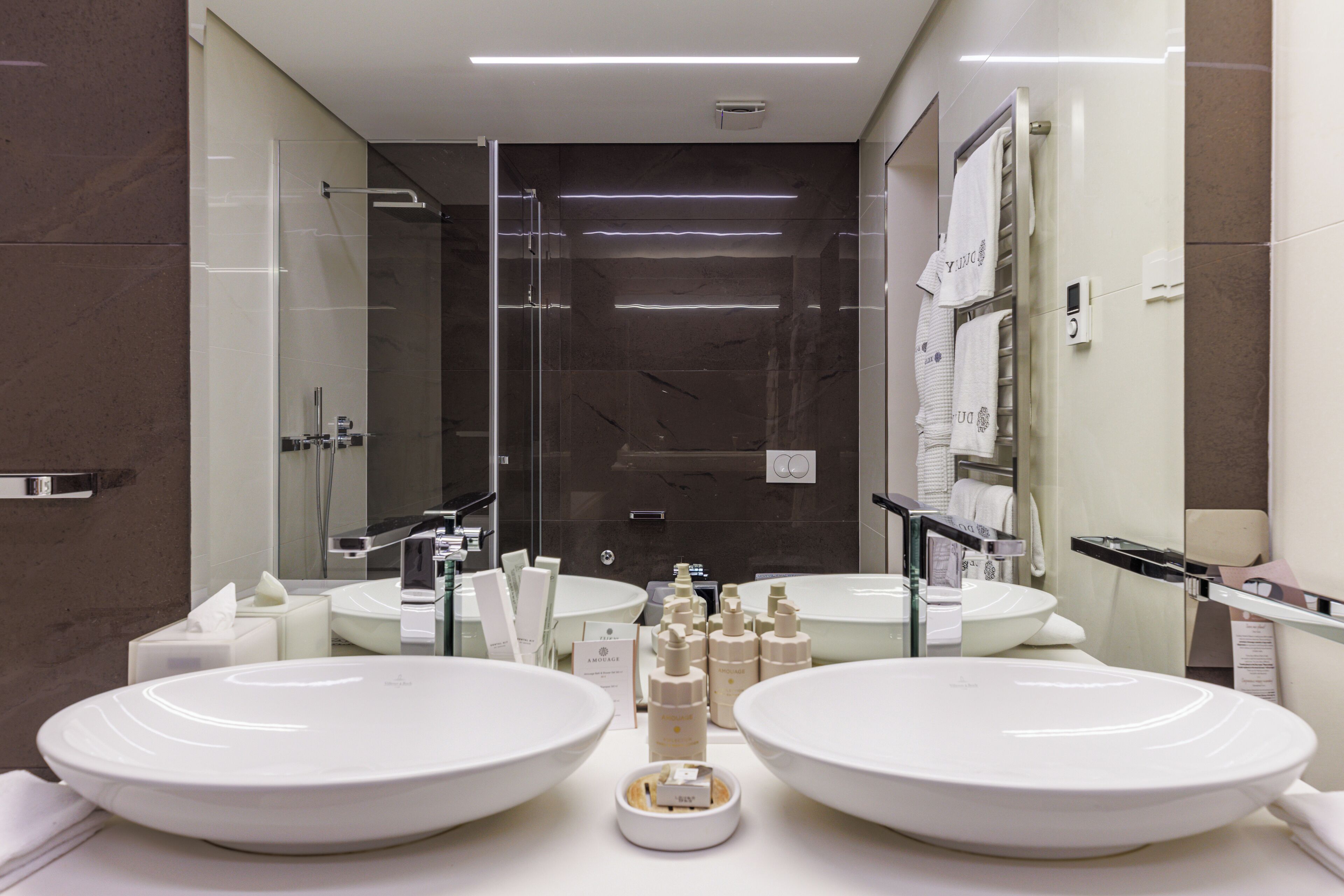 A modern bathroom with two large white sinks, a glass shower enclosure, and a mirror above the sinks.