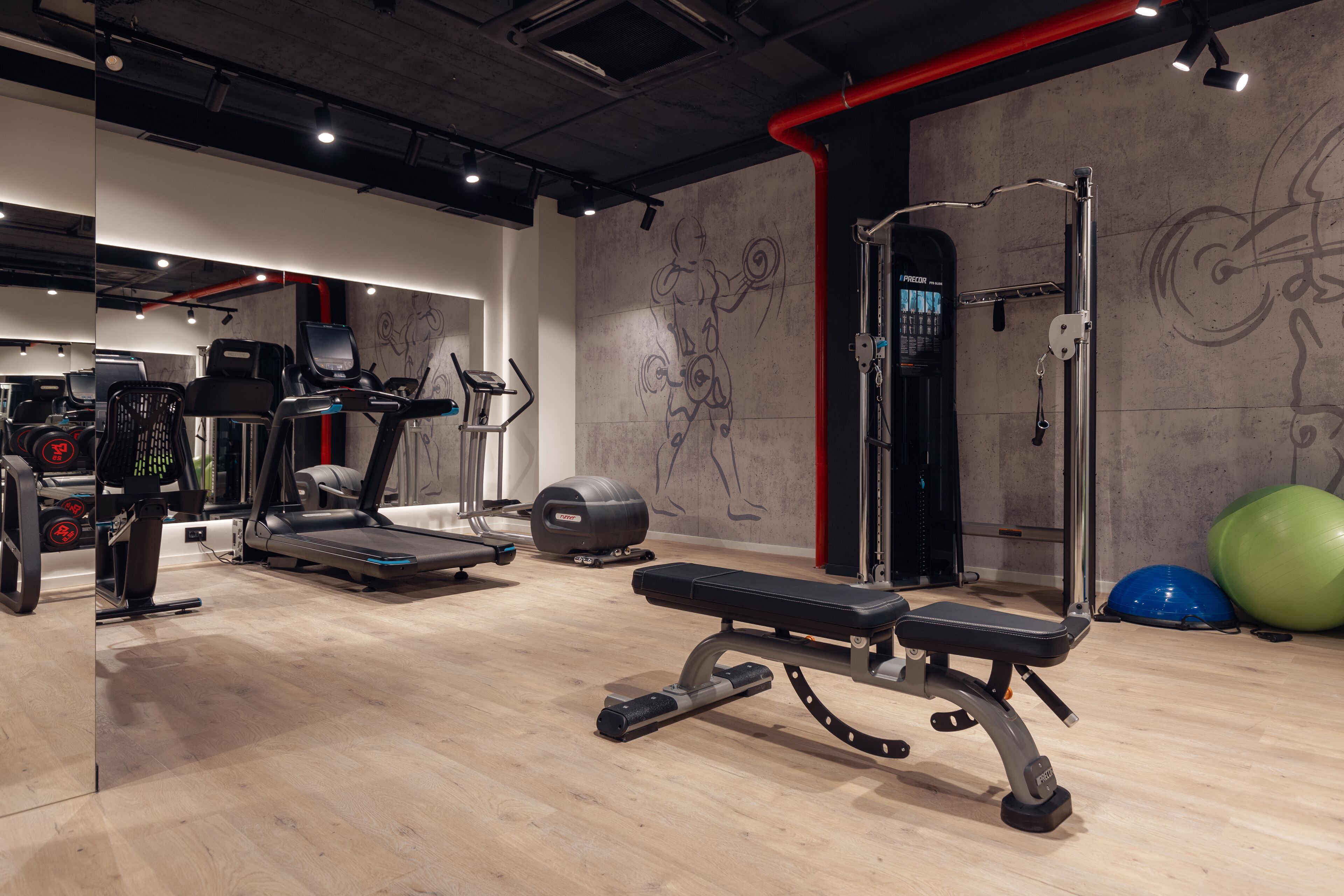 A gym with exercise equipment, a bench, and a wall with artistic designs.