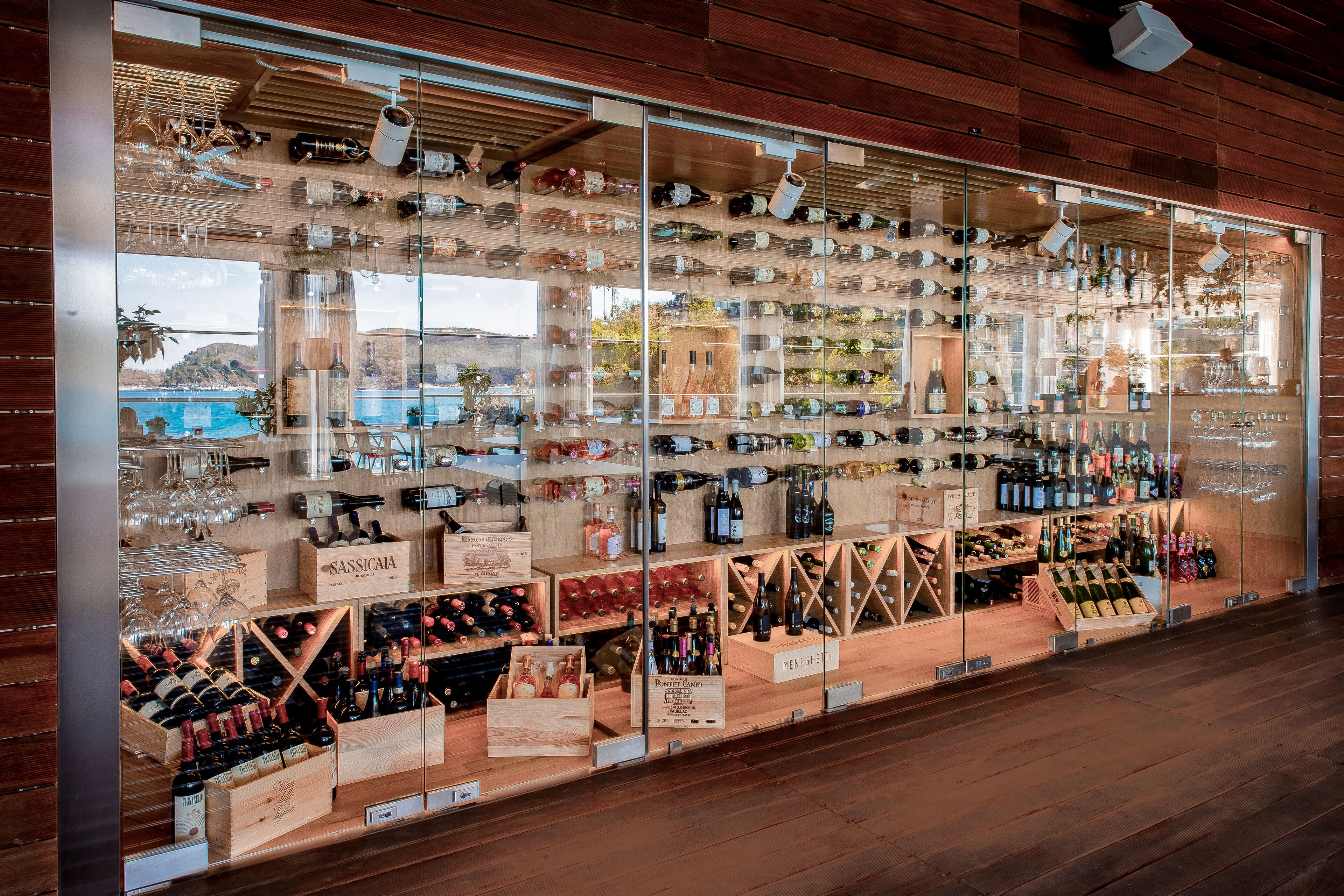 Una tienda de vinos con estanterías de madera y vitrinas de vidrio repletas de botellas y copas de diversos tipos.