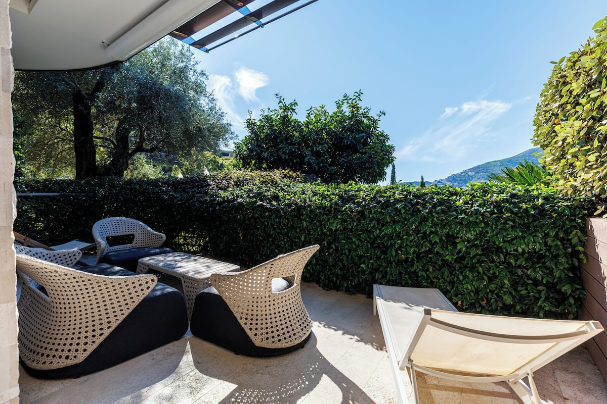 An outdoor seating area with wicker furniture, a table, and a view of a hedge and trees.