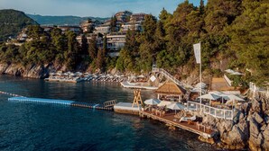 A coastal resort with multiple buildings, a pier, and a thatched-roof structure. - Dukley Hotel & Resort (Budva)
