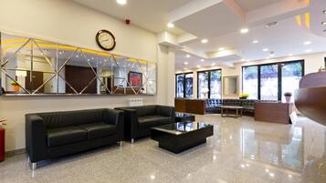 A modern lobby with a black leather sofa, a glass coffee table, and a large mirror with geometric patterns.
