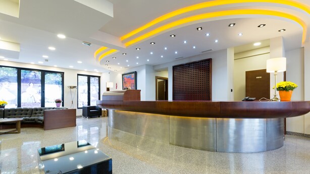 A modern reception area with a curved reception desk, a sofa, and a coffee table. - Sterling Hotel (Belgrade)